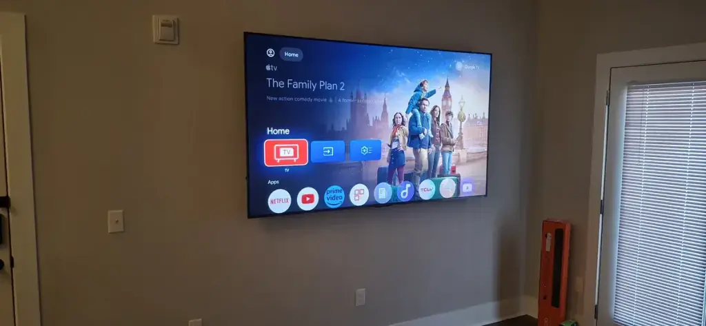 Wall mounted television showing the Google TV home screen with a row of streaming apps