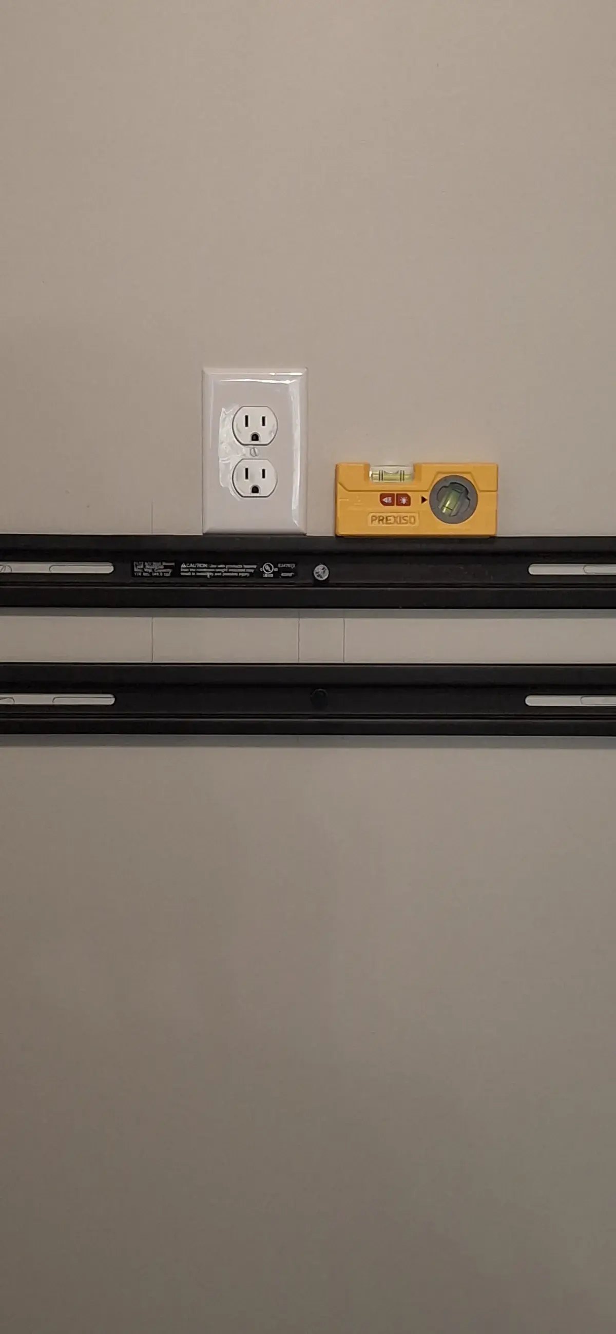 Close up of a wall outlet and a torpedo level staged on a TV mounting bracket rail