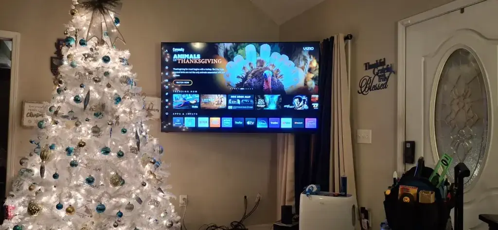 Television mounted over a fireplace beside a decorated Christmas tree in a family living room